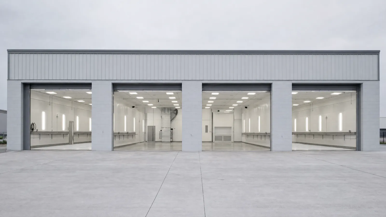 The shop seen from the apron early in the morning, the bay doors up and the bays lit and empty, no vehicles in the frame.